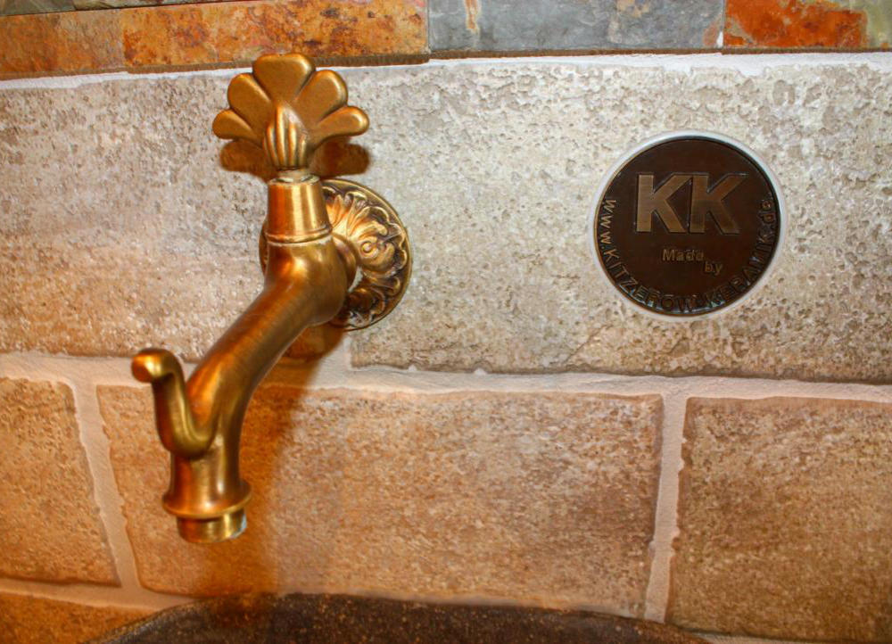 Messingarmatur mit graviertem Kitzerow-Keramik-Logo auf antikisierter Steinwand