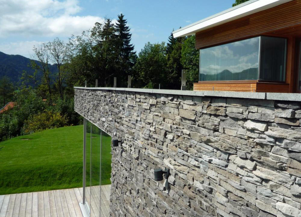 Modernes Wohnhaus mit Naturstein-Fassade vor Alpenpanorama